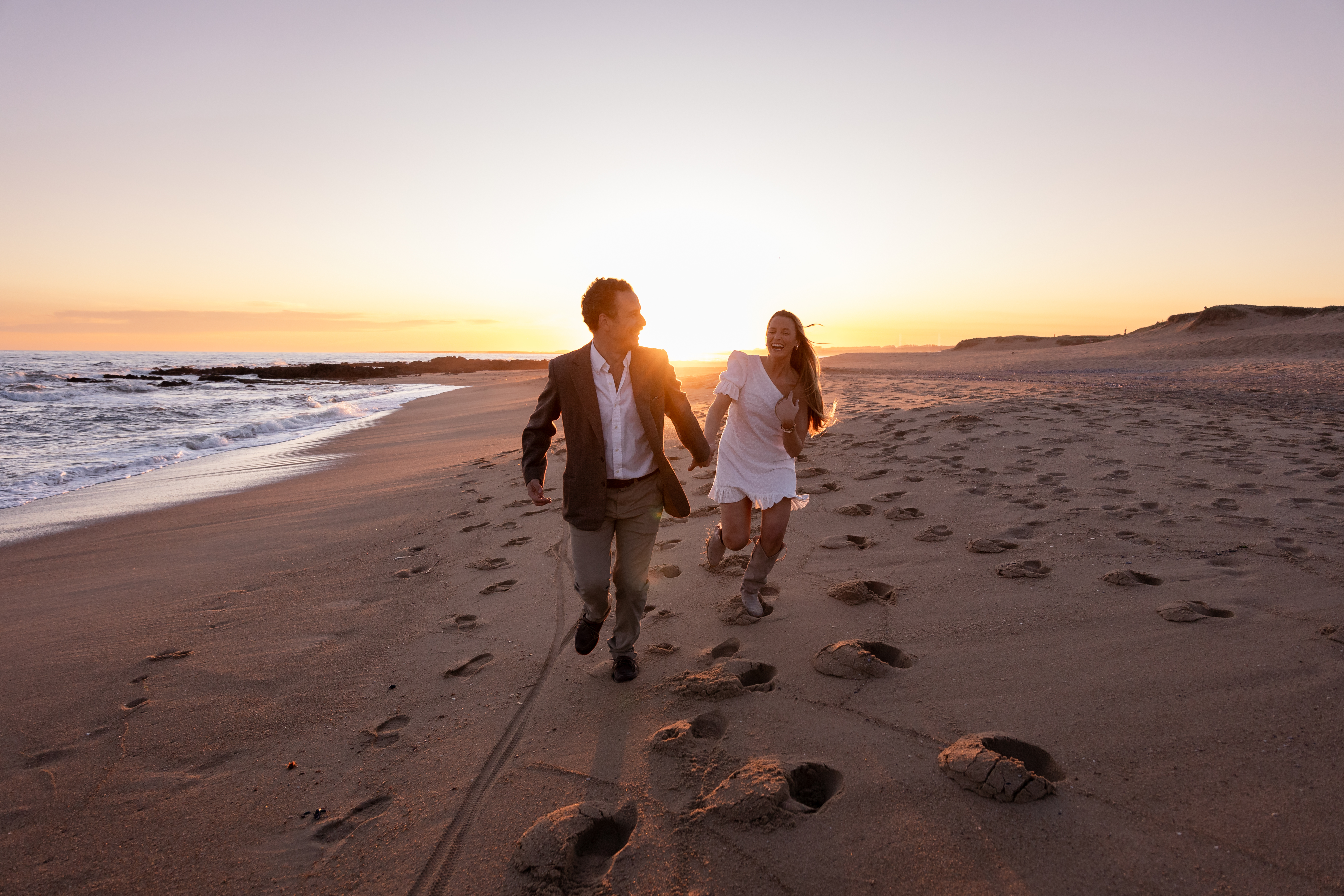 Pareja corriendo alegremente en la playa durante el atardecer